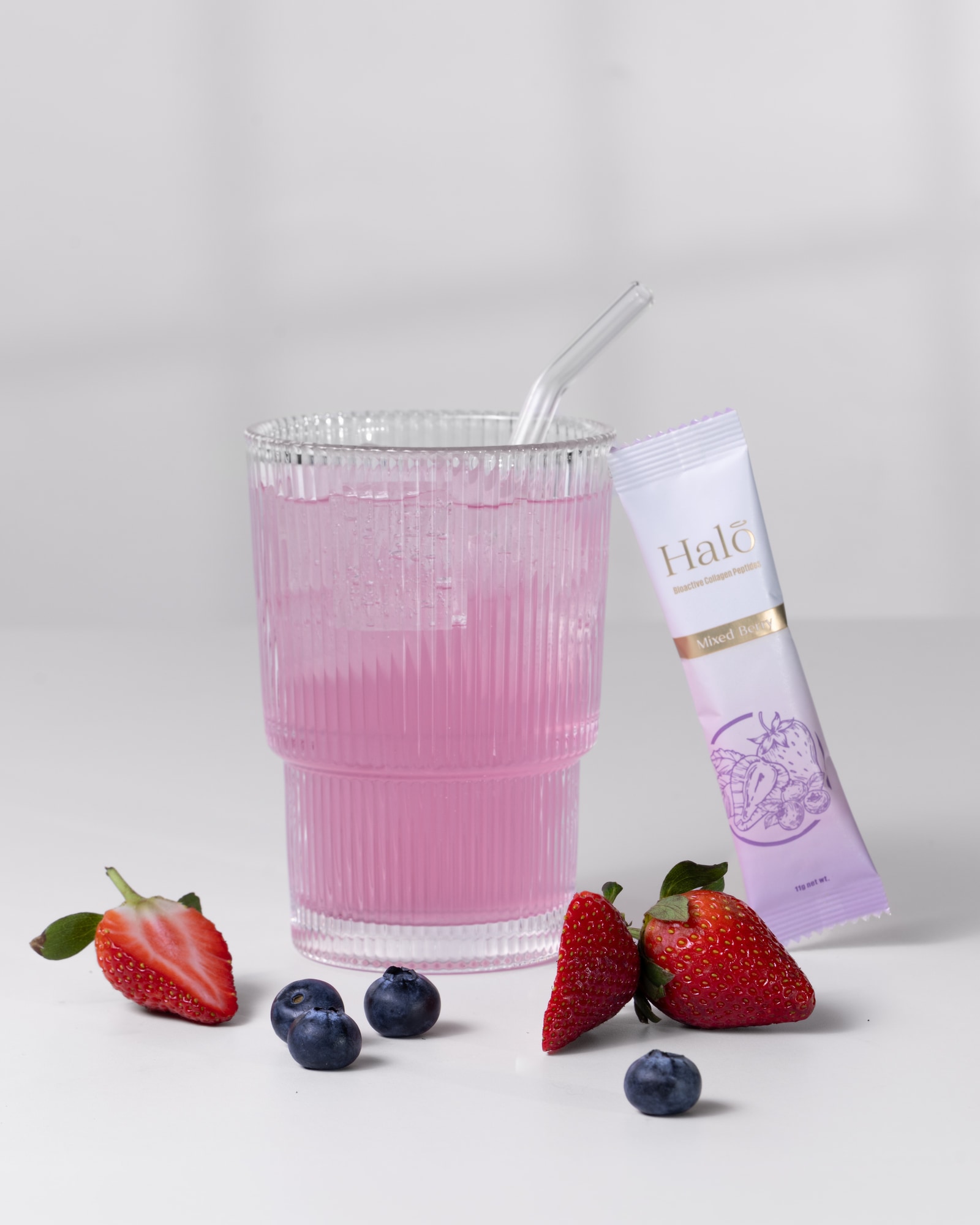 A Halo Mixed Berry sachet beside a pink drink with strawberries and blueberries