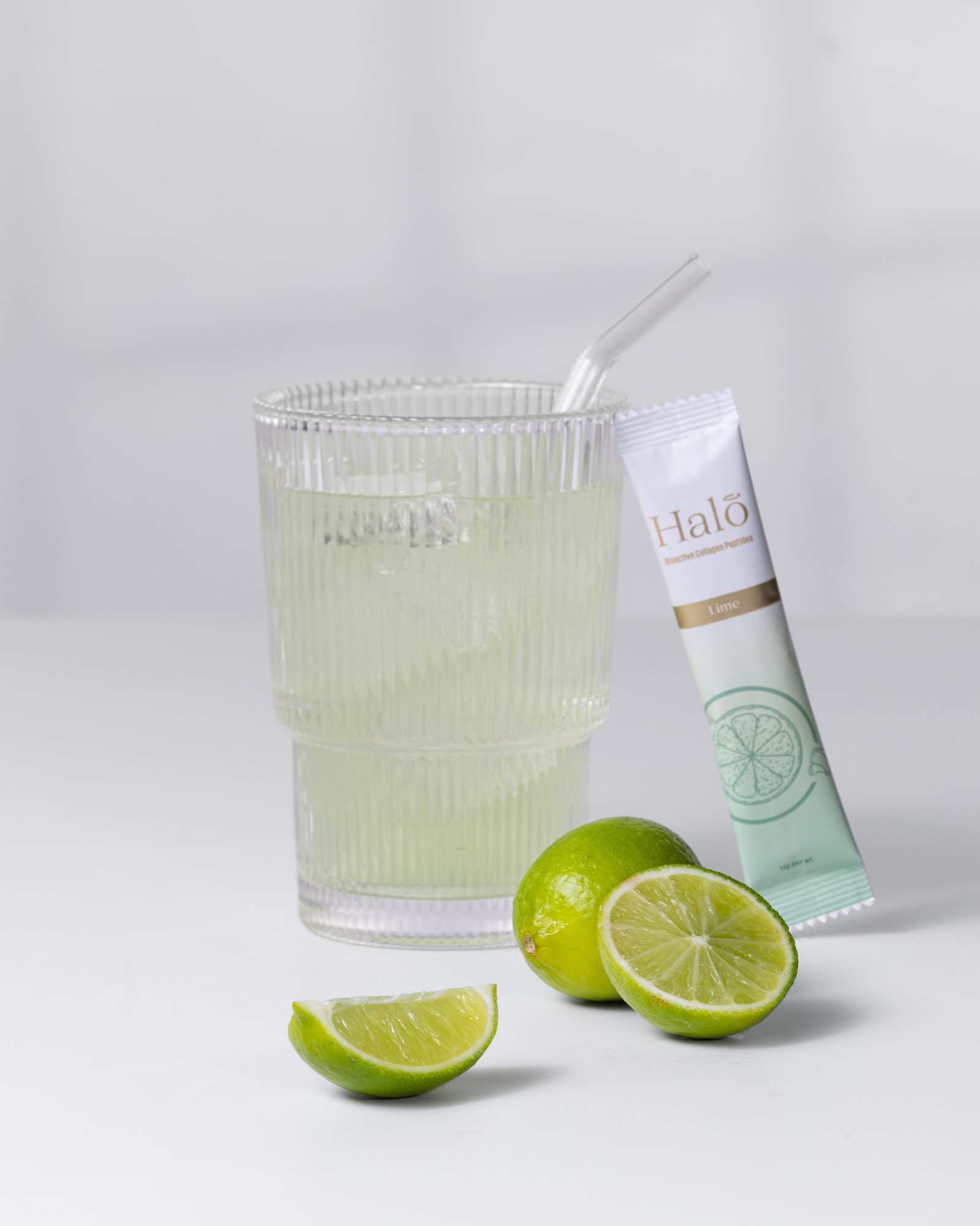 A Halo Lime sachet beside a glass of iced lime and fresh limes